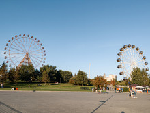Two Large Ferris Wheels In The Park On Mikhailovskaya Embankment After Reconstruction Against A Blue Sky And People Walking.