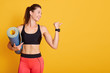 © sementsova321 - Profile portrait of young woman holding mat and shows muscles, sporty female looking aside, wearing stylish sportwear, poses smiling in studio isolatedover yellow background. Healthy lifestyle concept