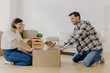 © VK Studio - Funny young woman and man have fun during relocation, pose on floor with dog in cardboard box, just moved into apartment, dressed in domestic clothes, sofa and pile of containers in background