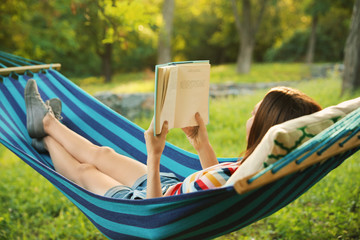 Poster - Young woman reading book in comfortable hammock at green garden