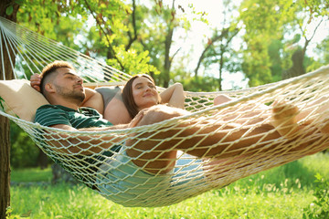 young couple resting in comfortable hammock at green garden