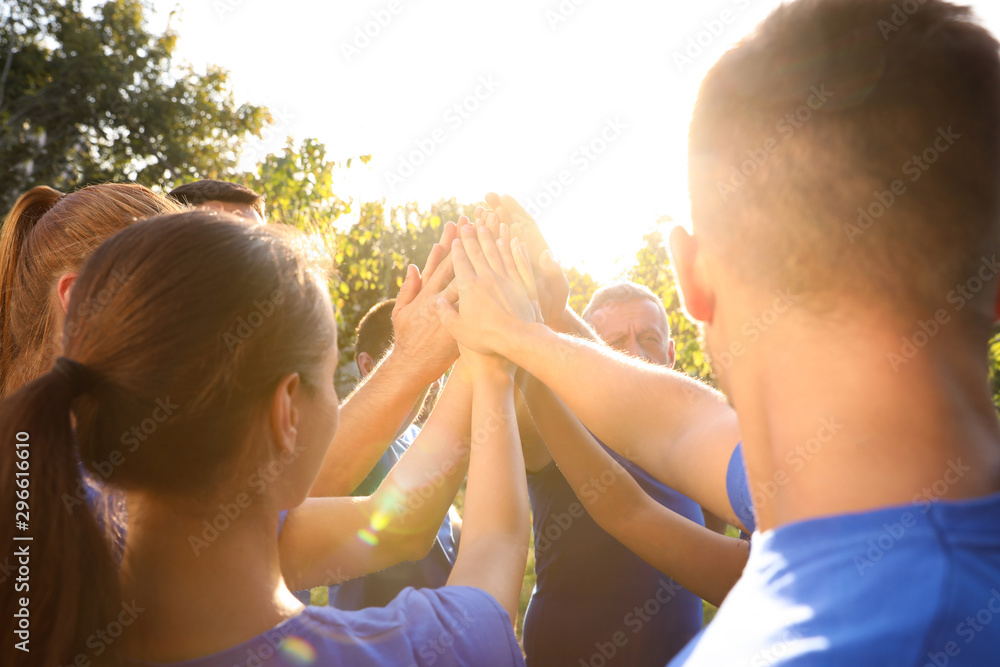 Group of volunteers joining hands together outdoors on sunny day - obrazy, fototapety, plakaty 