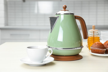 Poster - Modern electric kettle, cup and muffins on wooden table in kitchen