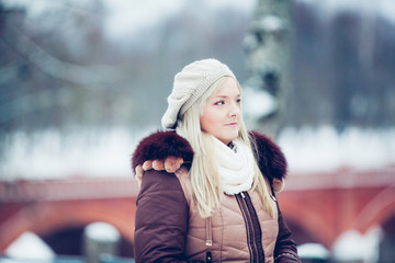 Amazing portrait of cute blonde European Latvian woman looking happy in winter. Wearing white faux fur scarf and dark brown jacket and headpiece