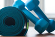 A blue rolled yoga mat. Two blue 2 kg dumbells resting on it. Fitness equipment for home exercise and flexibility training.