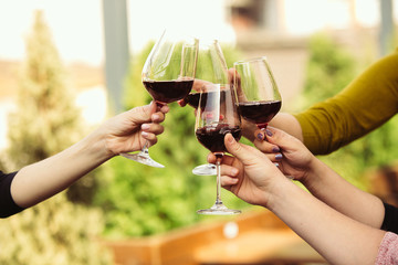 People clinking glasses with wine on the summer terrace of cafe or restaurant. Happy cheerful friends celebrate summer or autumn fest. Close up shot of human hands, lifestyle.