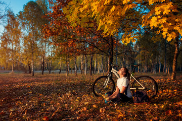 Wall Mural - Riding bicycle in autumn forest. Young woman biker relaxing after exercising on bike. Healthy lifestyle