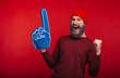 Amazed bearded hipster man standing over red background and celebrating success with fan finger glove