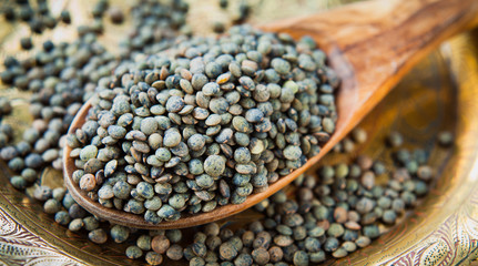 Puy Lentils -  French Green legume, dried grains on wooden spoon.