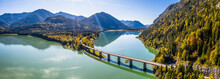 Scenic Aerial View Of The Bridge Over Lake Sylvenstein With Beautiful Reflections. Alps Karwendel Mountains In The Back. Autumn Scenery Of Bavaria, Germany