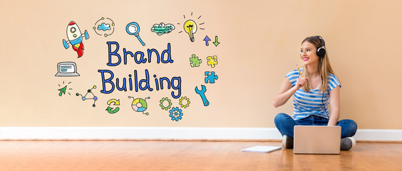 Wall Mural - Brand building with young woman with headphones using a laptop computer and a pencil