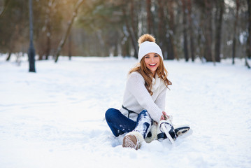 Wall Mural - Young woman sits on the frosty snow in winter park. Winter holidays concept.