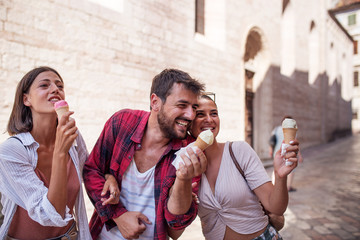 Wall Mural - View of three happy friends talking and eating ice creams walking in the street