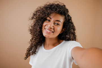 lovely happy black young woman making selfie isolated over brown