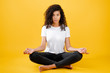 relaxed black woman meditating in yoga pose isolated over yellow