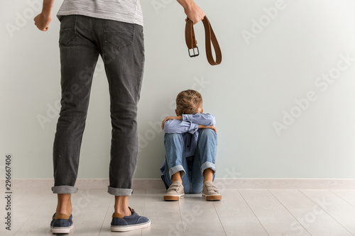 Fotografía Man threatening his little son who is sitting on floor near light wall
