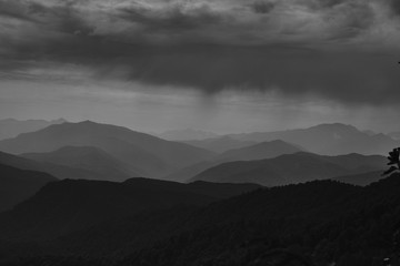 Sticker - Beautiful shot of forested hills and mountains under a cloudy sky in black and white