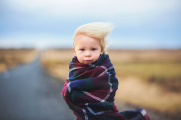 Beautiful child, standing on a road on a very windy day, wrapped in scarf, watching the sunrise in Iceland