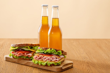 Wall Mural - fresh sandwiches with lettuce, ham, cheese, bacon and tomato near bottles of beer at wooden table isolated on beige