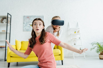 Wall Mural - surprised babysitter with outstretched hands near kid in virtual reality headset