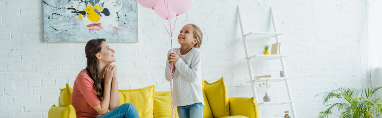 Wall Mural - panoramic shot of cheerful babysitter looking at pink balloons near happy kid