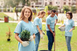 © Viktoriia - Volunteering. Young people volunteers outdoors planting trees girl standing with pot close-up looking camera cheerful blurred background