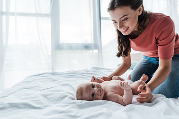 Wall Mural - happy mother looking at infant daughter lying on bed