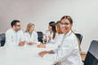 © bnenin - Medical meeting. One female doctor looking at camera. Colleagues talking in the background.