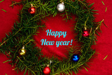 Inscription Happy New Year Placed In A Wreath From A Christmas Tree With Balls On A Red Background With A Top View