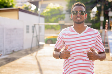 Wall Mural - Happy young African man with sunglasses giving thumbs up outdoors