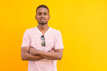 Wall Mural - Happy young African bearded man smiling with arms crossed against yellow wall