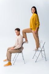 Wall Mural - cheerful girl standing on chair near handsome man sitting on white