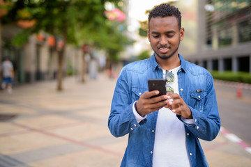 Wall Mural - Happy young African bearded man using phone in the city streets