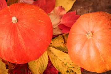 Two orange pumpkins and autumn foliage on a wooden surface.