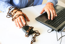 Man's Hands In Old Rusty Chains. In The Trap Of Office Work. Routine Job. Manager Near The Laptop.