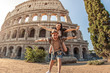 Young happy couple having fun at Colosseum, Rome. Piggyback posing for pictures.