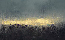A Window With Fogged Glass. Autumn Rainy Morning Landscape Is Seen - A Bright Strip Between Heavy Blue Clouds.