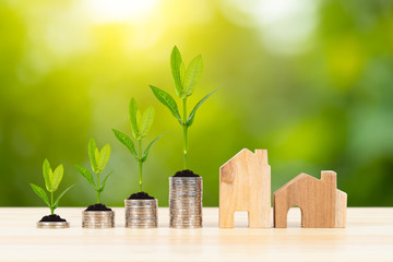 Wall Mural - Coin stack and model house with growing leaves on wooden desk on green tree background, mortgage concept