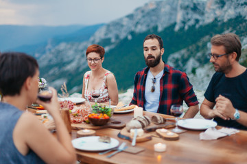 Wall Mural - Friends and family gathered for picnic dinner for Thanksgiving. Festive young people celebrating life with red wine, grapes, cheese platter, and a selection of cold meats