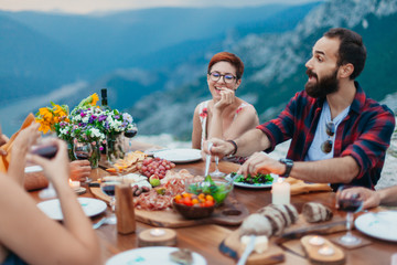 Wall Mural - Friends and family gathered for picnic dinner for Thanksgiving. Festive young people celebrating life with red wine, grapes, cheese platter, and a selection of cold meats