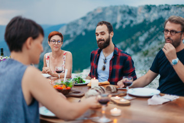 Wall Mural - Friends and family gathered for picnic dinner for Thanksgiving. Festive young people celebrating life with red wine, grapes, cheese platter, and a selection of cold meats