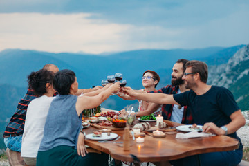 Wall Mural - Friends and family gathered for picnic dinner for Thanksgiving. Festive young people celebrating life with red wine, grapes, cheese platter, and a selection of cold meats