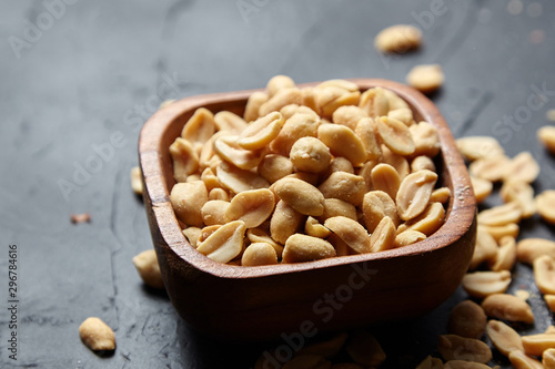 Fotografía Wooden bowl with roasted peeled peanuts, salty beer snack on dark background