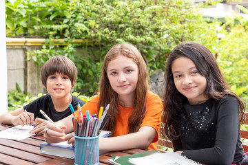 Children, boy and girl, doing homework and drawing together in garden at home, looking at camera