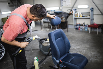 An auto service worker prepares and cleans the car seat