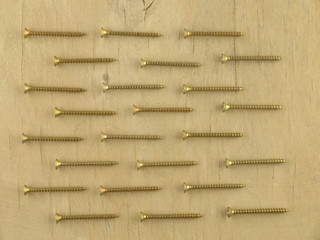  golden screws laid out on a wooden board.Flat lay