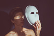 Close-up portrait of young woman, she is holding white mask, mask shadow on face. Tone photo
