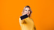 © Alexander - Cute young woman in a yellow sweater holding a smartphone