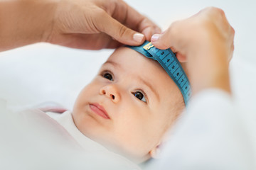 medicine, healthcare and pediatrics concept - female pediatrician doctor with measure tape measuring baby girl patient's head at clinic or hospital