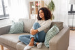people, race, ethnicity and portrait concept - happy african american young woman sitting on sofa at home